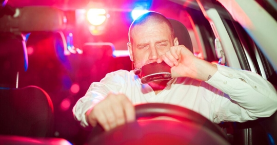 man driving with flask and police lights behind
